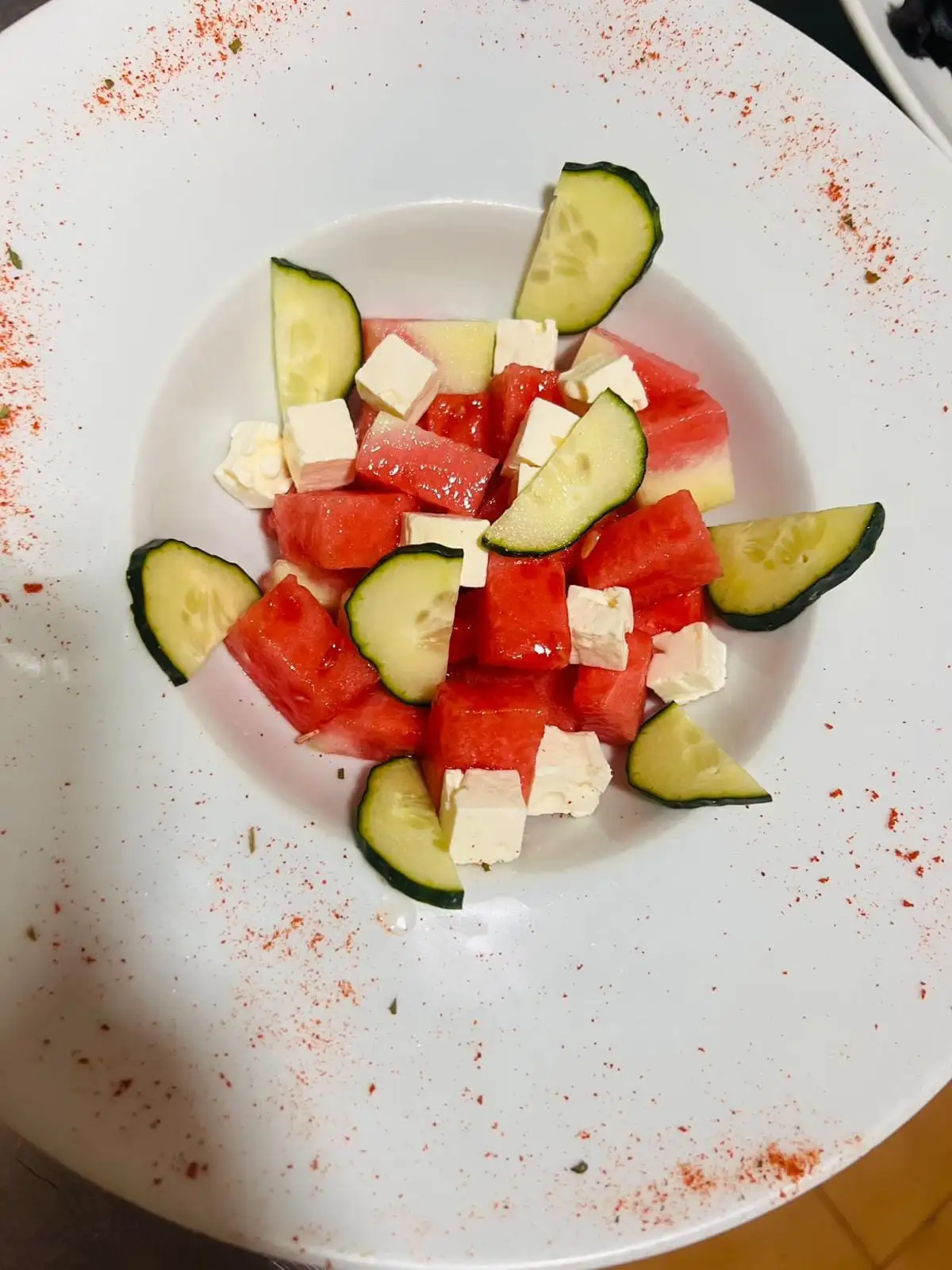 Ensalada de sandía con dados de queso feta y rodajas de pepino, en un plato blanco.