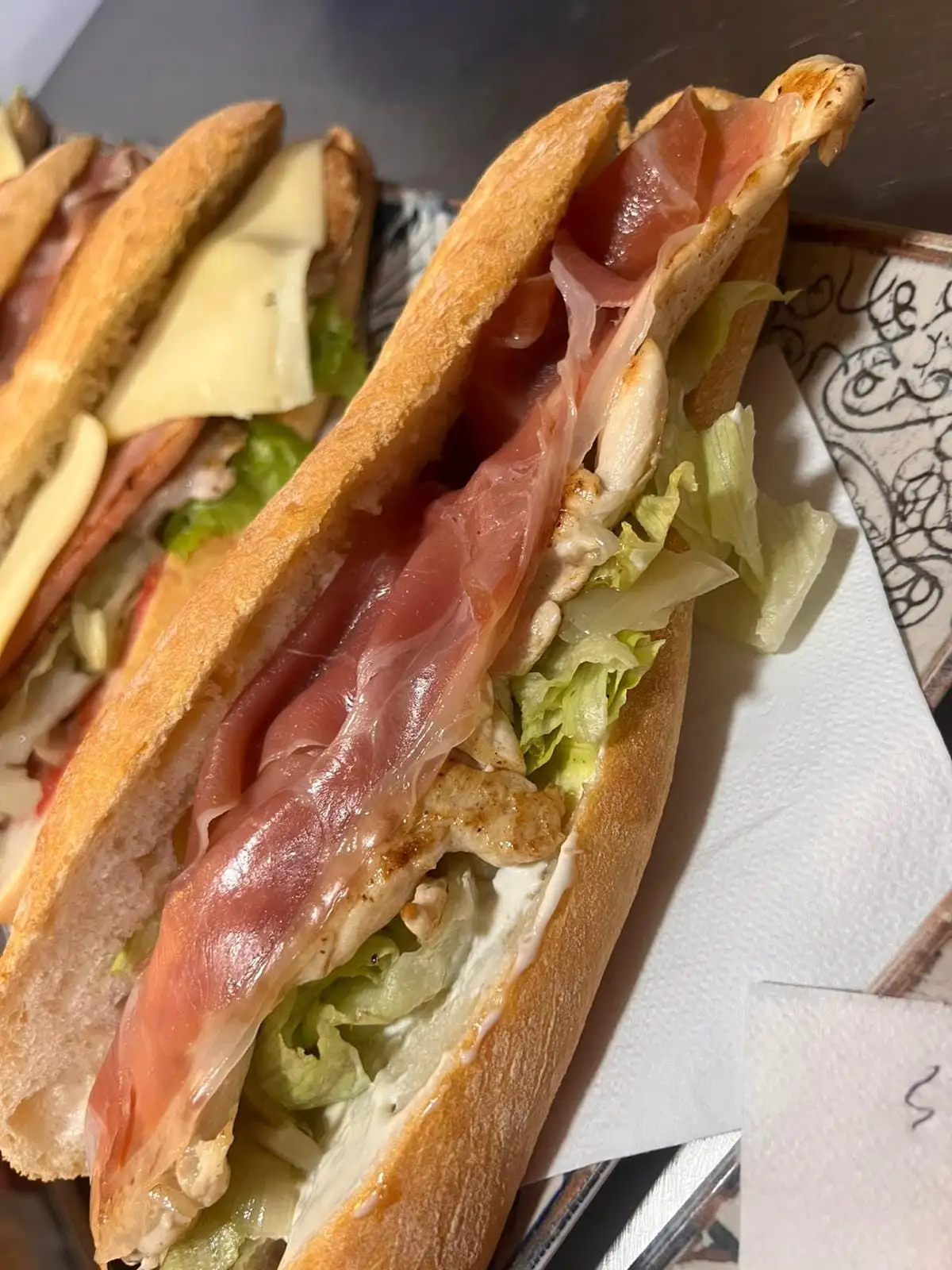 Bocadillo de barra abierto con jamón serrano, filetes a la plancha, lechuga y mayonesa asomando por el pan.