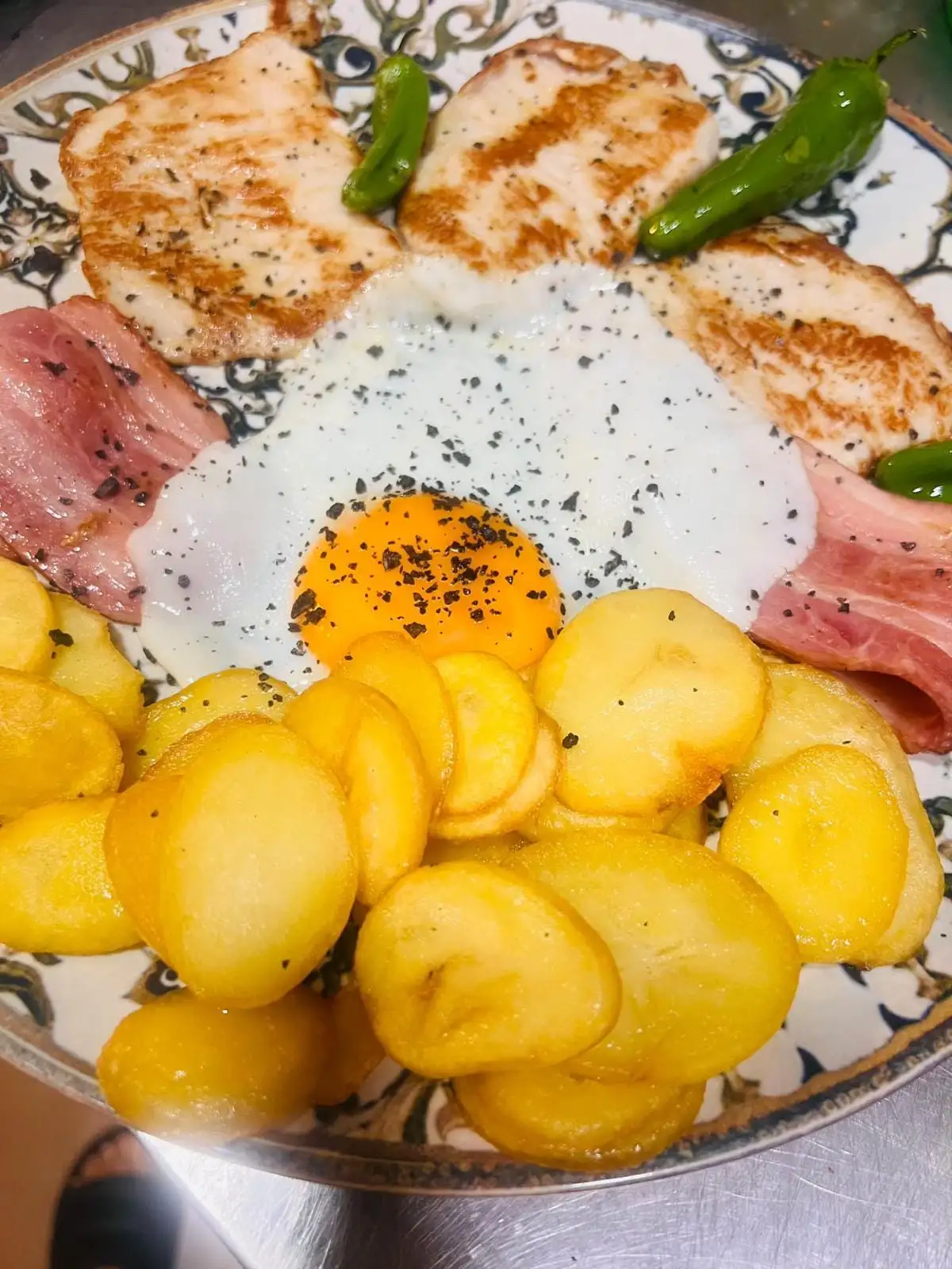 Plato con filetes a la plancha, lonchas de bacon, huevo frito, patatas en rodajas y pimientos verdes.