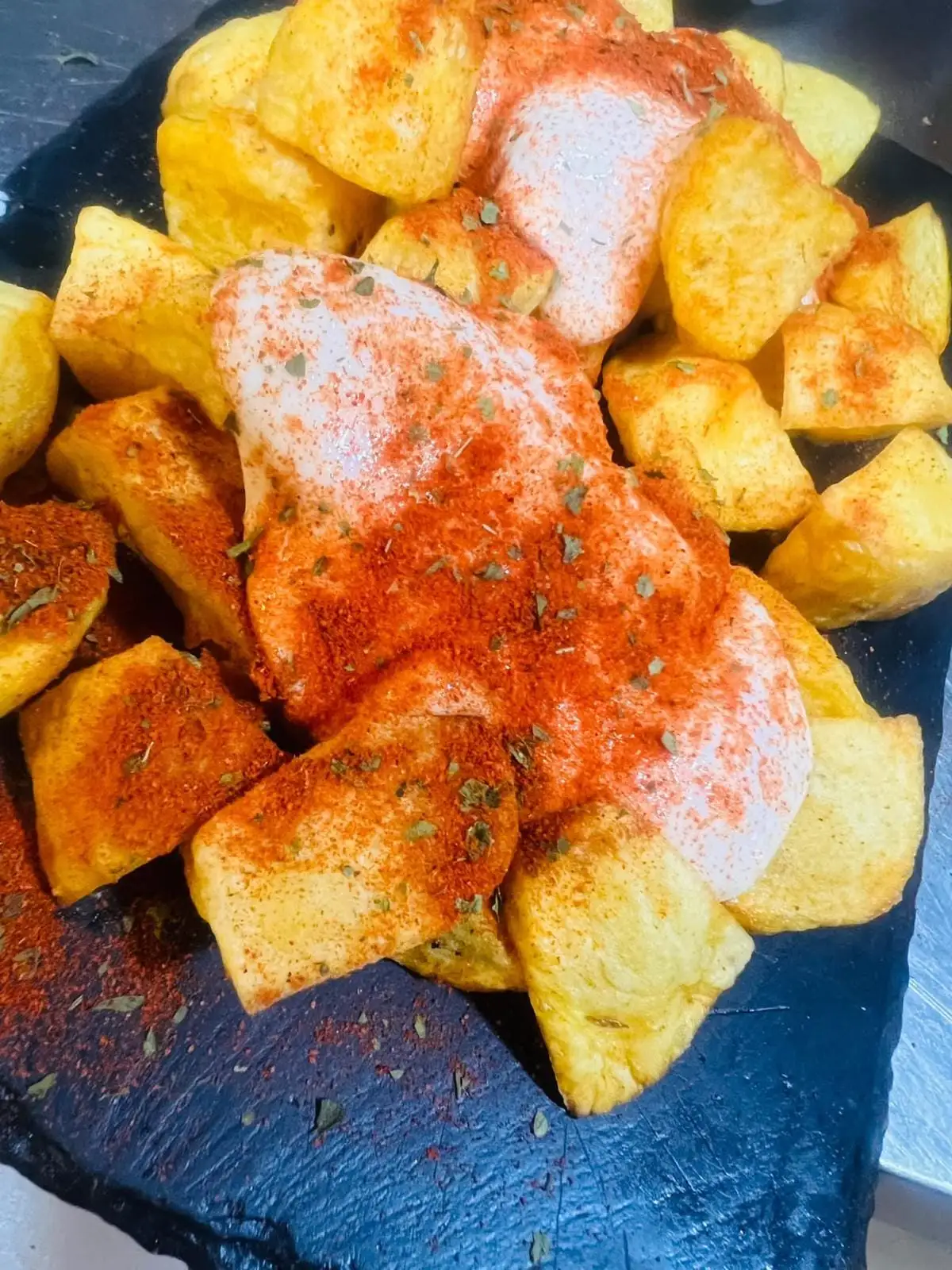 Patatas fritas en tacos sobre una pizarra, con salsa blanca, pimentón y orégano por encima.