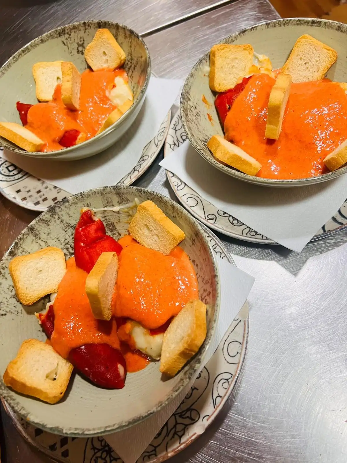 Tres cuencos con pimientos rojos asados y queso bañados en una crema de tomate, con rebanadas de pan tostado en el borde.