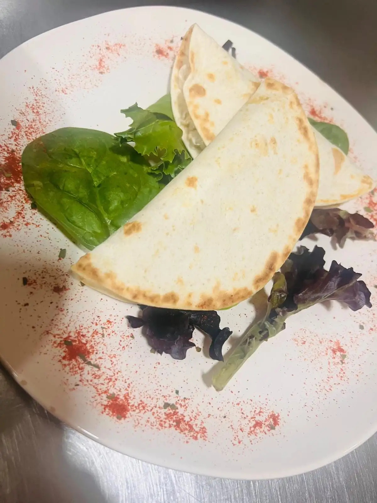 Dos tortillas de trigo dobladas y tostadas en un plato blanco, con hojas de ensalada variadas y pimentón espolvoreado.