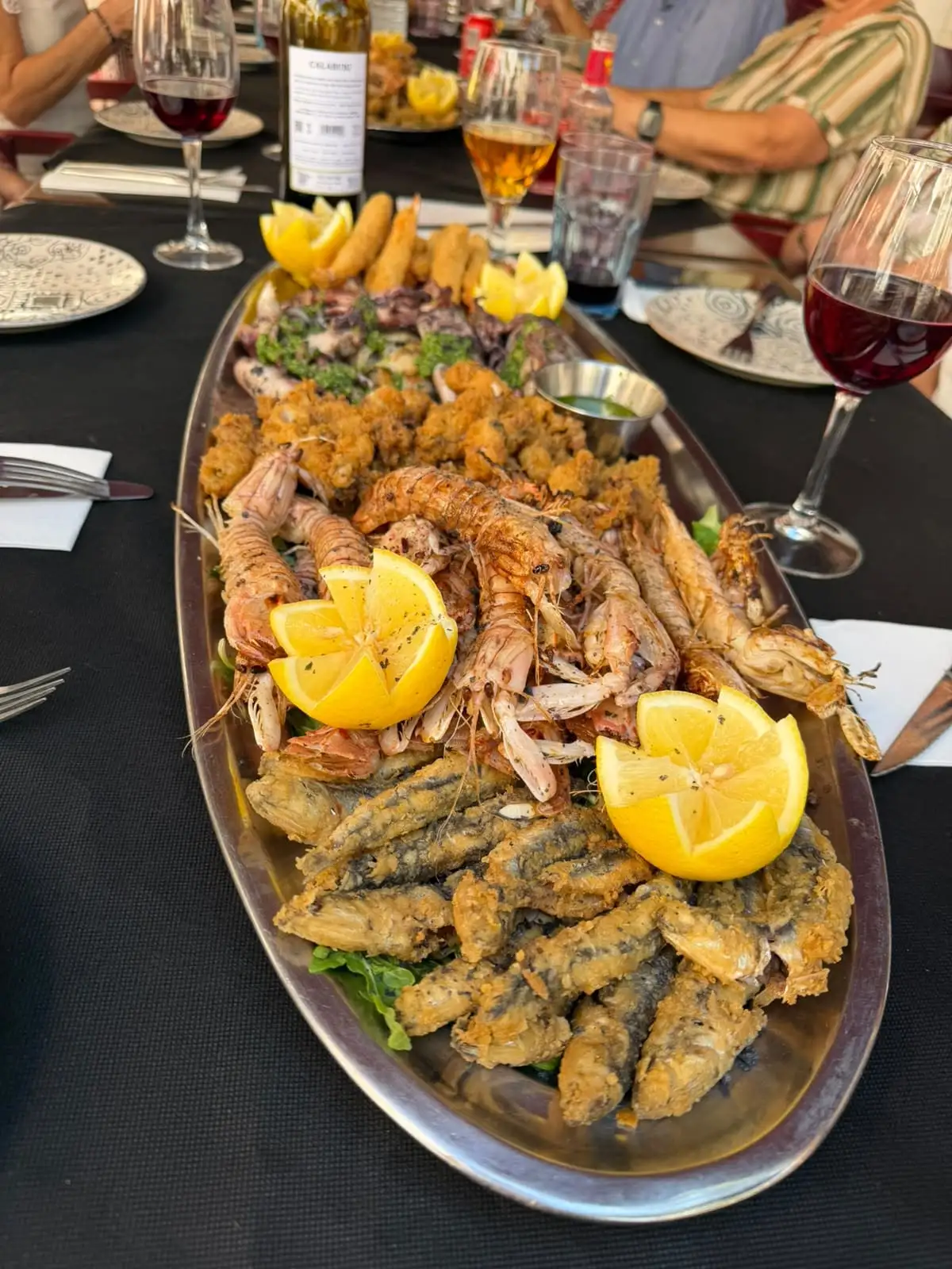 Fuente ovalada de marisco en el centro de la mesa: galeras y gambas a la plancha, boquerones y calamares fritos, limón y una cazuelita de salsa verde.