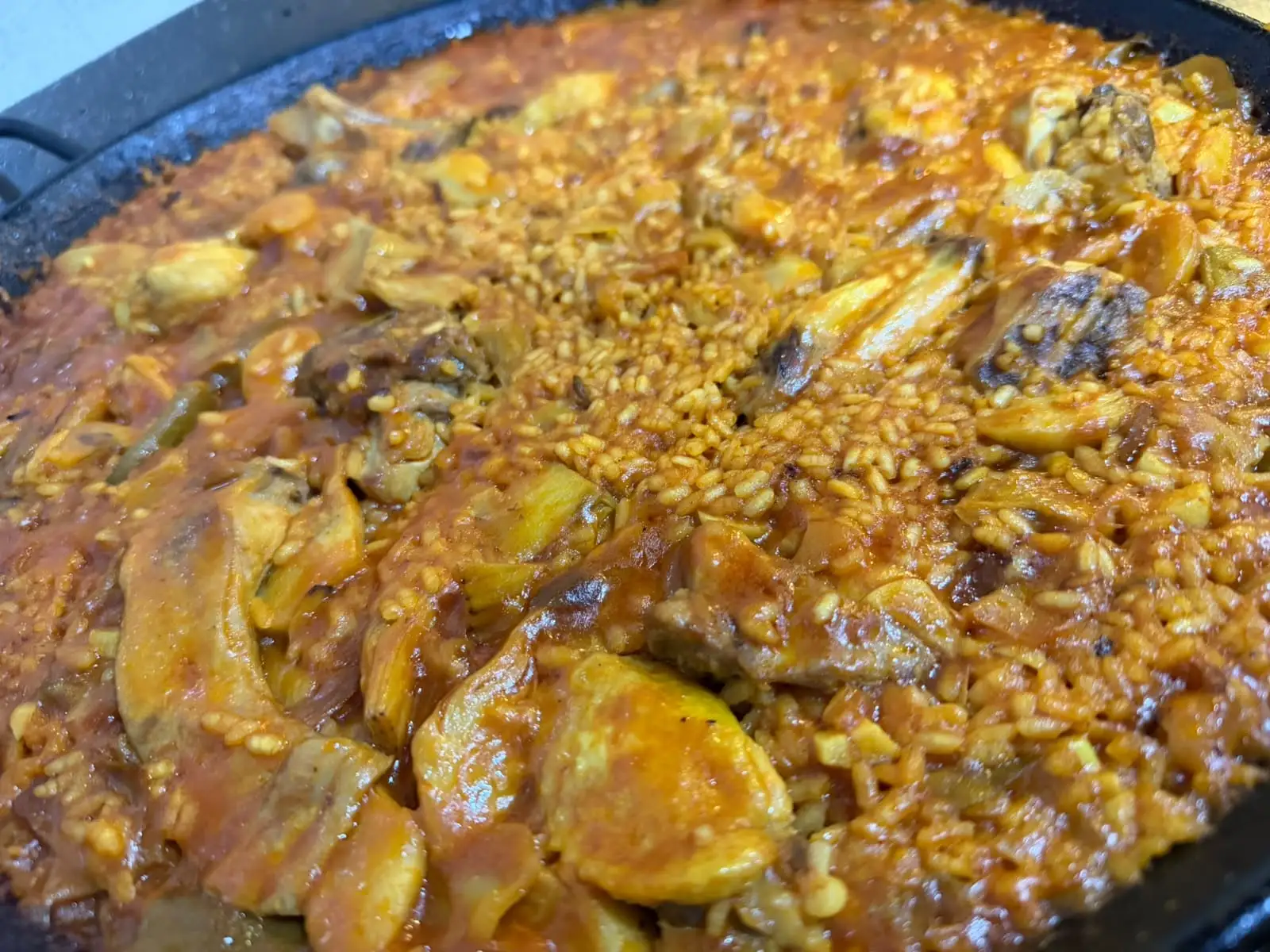 Primer plano de un arroz jugoso en la paella, con trozos de carne y alcachofa entre el grano.