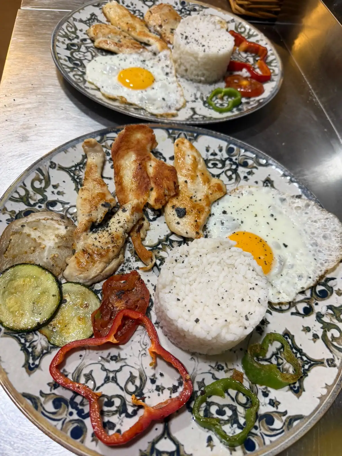 Dos platos de loza decorada con tiras de carne a la plancha, huevo frito, un molde de arroz blanco y verduras asadas.