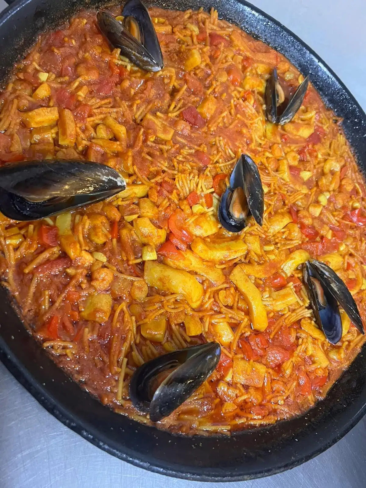 Fideuá en la paella, con mejillones abiertos y tiras de pimiento rojo entre los fideos.