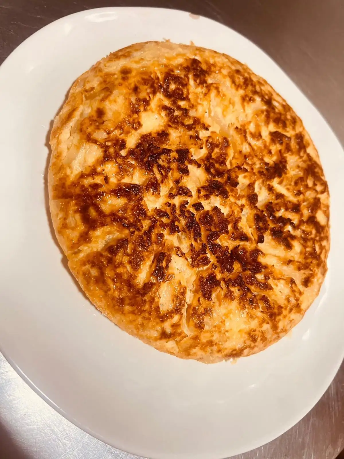 Tortilla de patatas entera y bien dorada, servida en un plato blanco ovalado.