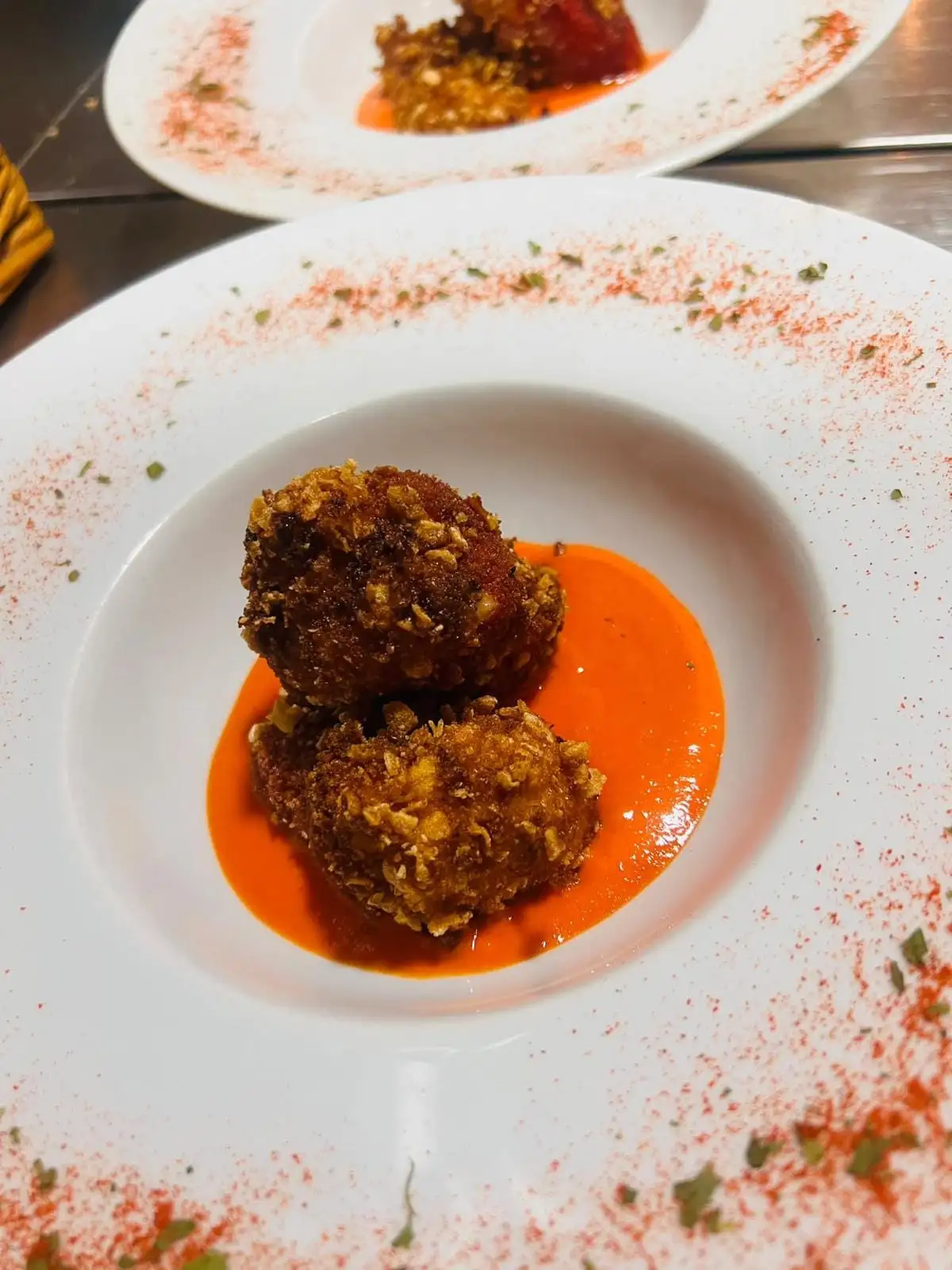 Dos croquetas de rebozado crujiente sobre un fondo de salsa anaranjada, en un plato hondo con pimentón espolvoreado en el borde.