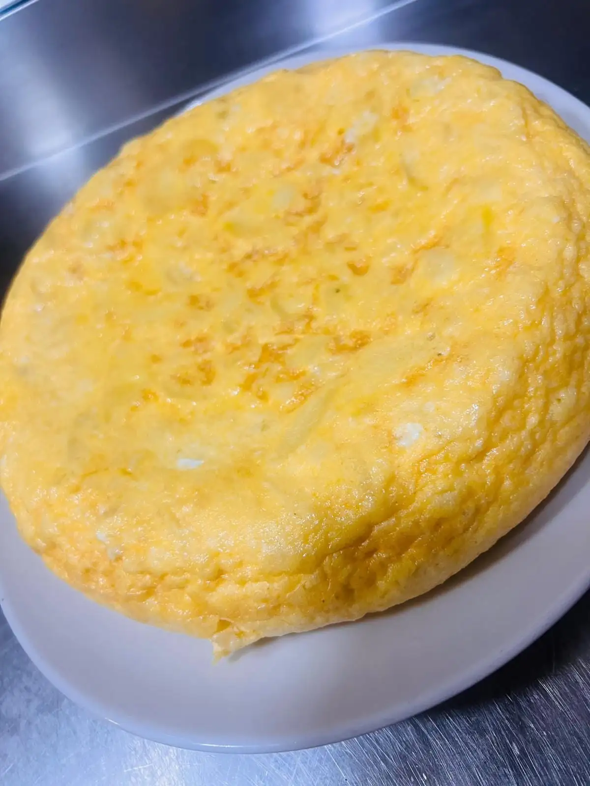 Tortilla de patatas alta y poco cuajada, servida entera en un plato blanco.