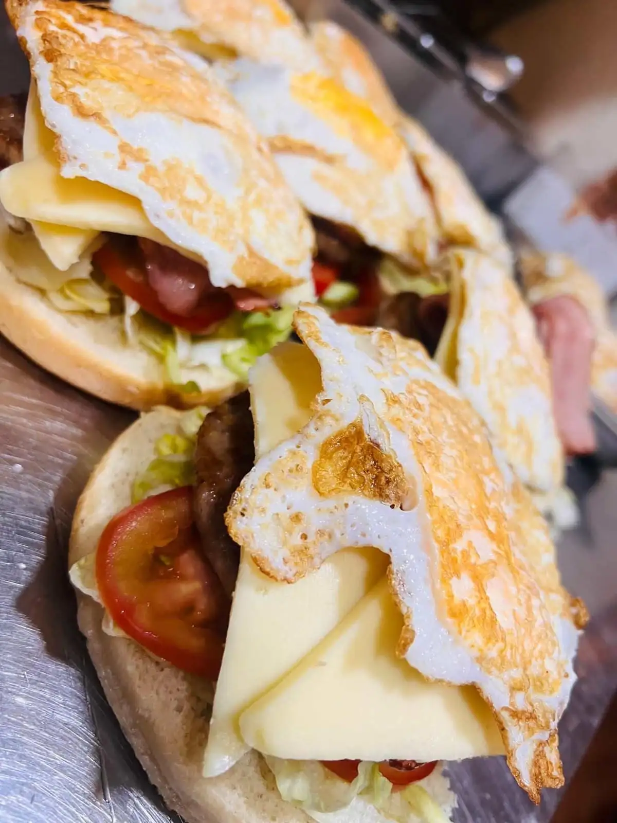 Bocadillos de pan redondo abiertos, con lechuga, tomate, carne a la plancha, lonchas de queso y un huevo frito coronando cada uno.