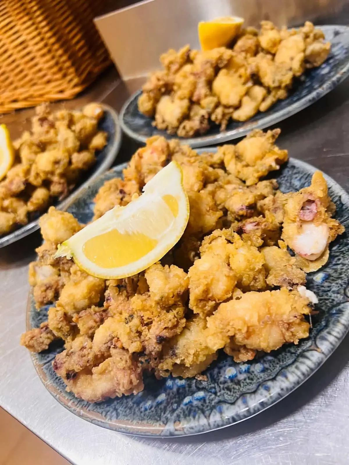 Tres platos de loza azul moteada con calamares rebozados y fritos, cada uno con una cuña de limón encima.