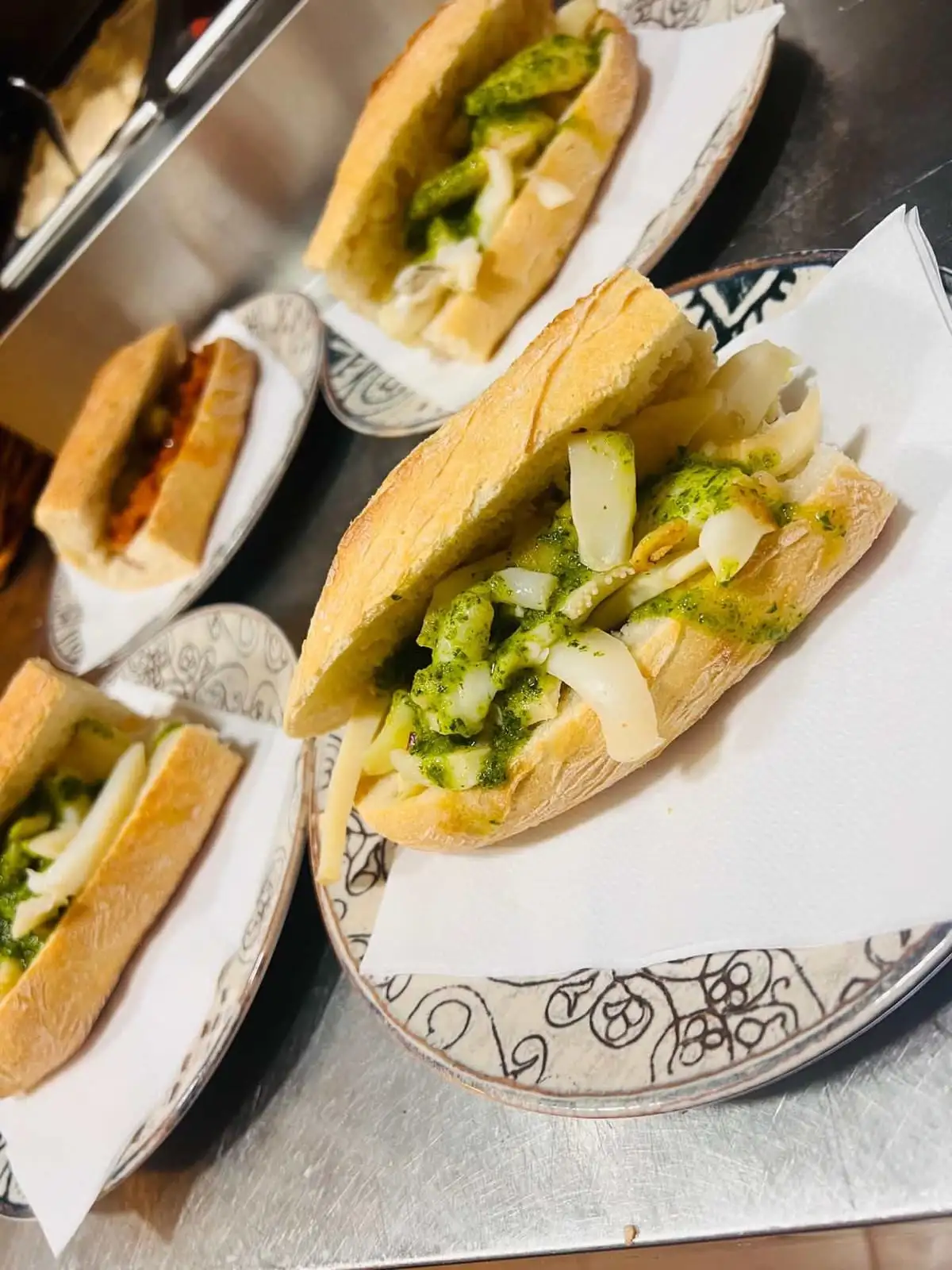 Varios bocadillos de sepia en salsa verde de perejil, servidos sobre servilleta en platos de cerámica decorada.