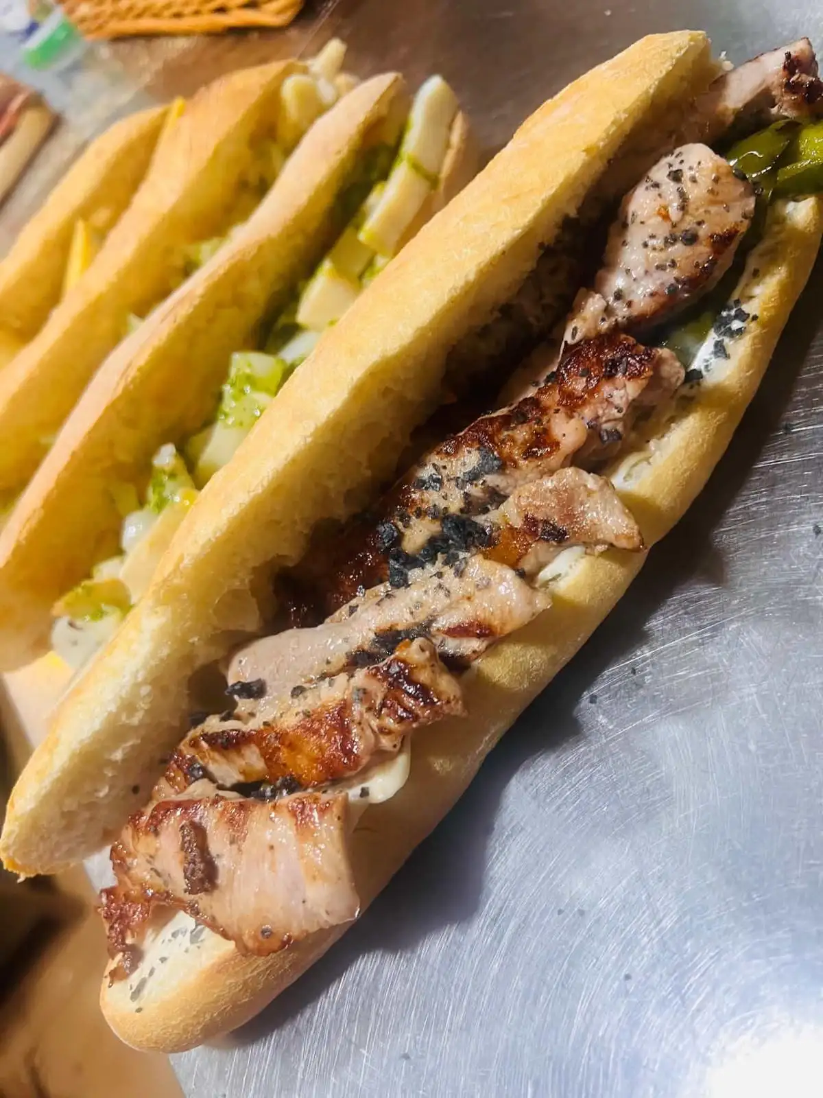 Bocadillo de barra con filetes de lomo a la plancha y pimienta negra, y al fondo otros dos con lechuga y queso.