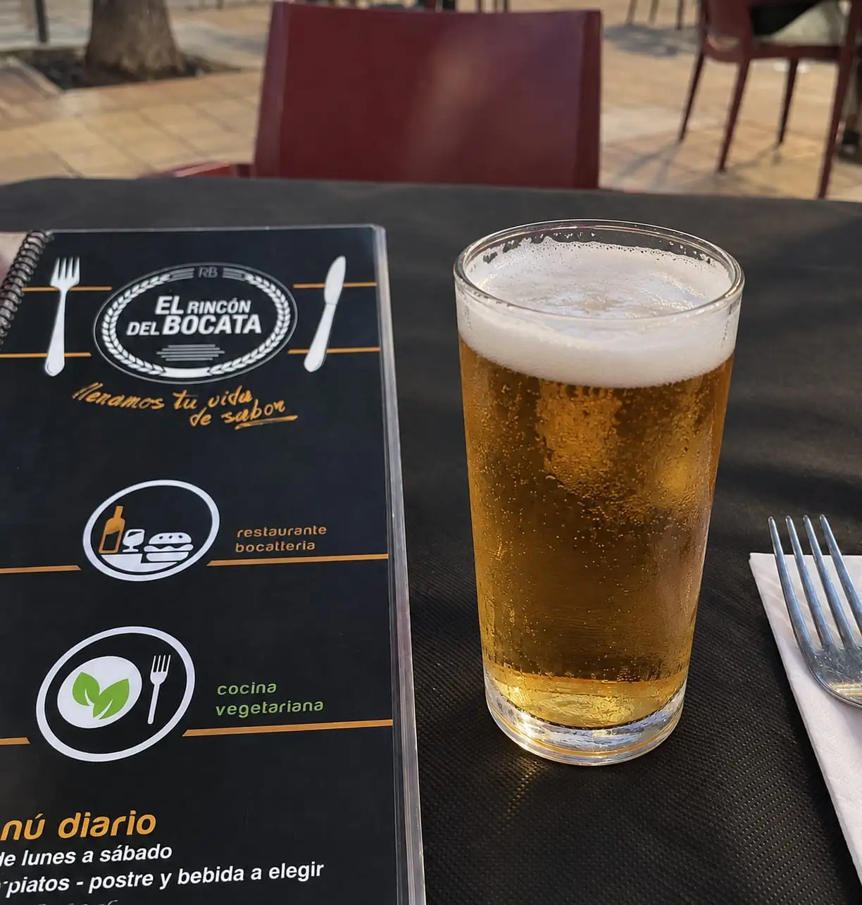 Caña de cerveza con espuma en la mesa de la terraza, junto a la carta del restaurante abierta por la portada.
