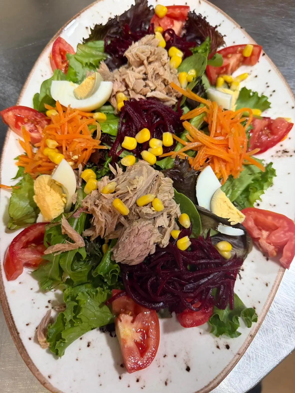 Ensalada mixta servida en plato ovalado: lechuga, tomate, zanahoria y remolacha ralladas, maíz, huevo duro y atún.