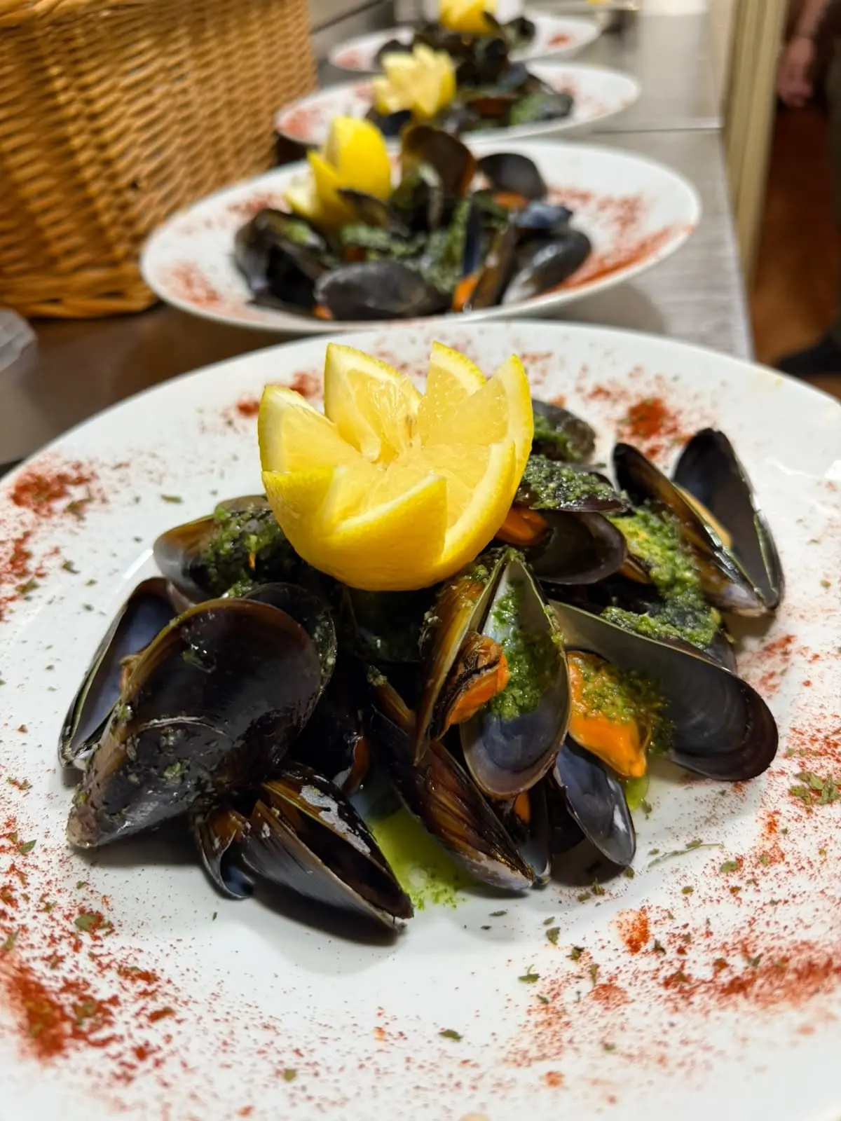 Plato de mejillones al vapor con salsa verde y un limón tallado encima.