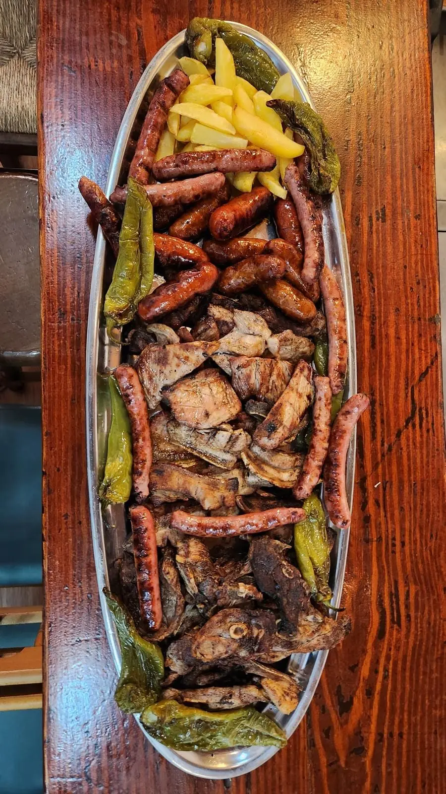 Parrillada de carne en bandeja ovalada: longaniza, chorizo, costilla y lomo a la brasa, con patatas fritas y pimientos verdes.