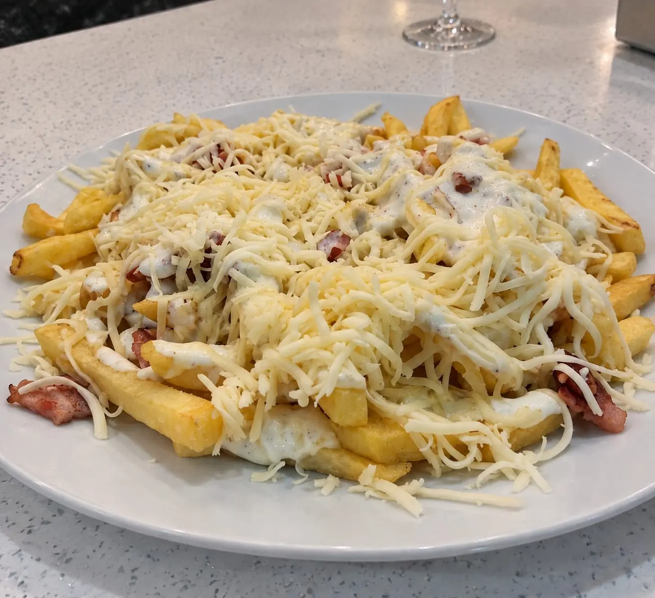 Fuente de patatas fritas con queso rallado, bacon y salsa por encima.