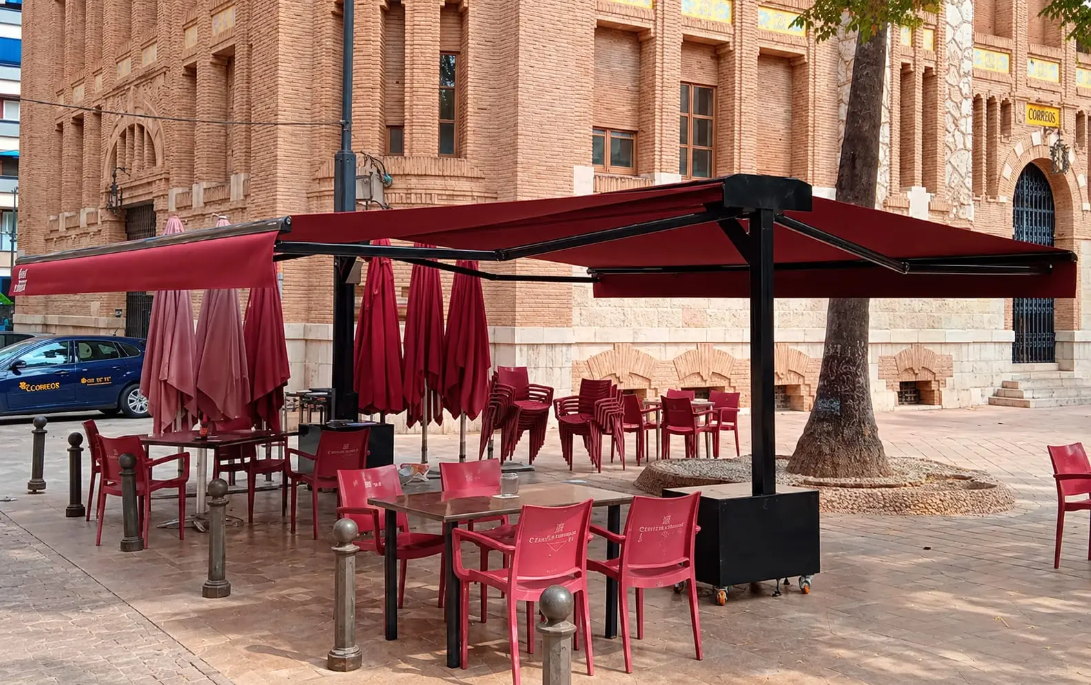 La terraza en la plaza Tetuán: mesas y sillas granates bajo dos toldos, con el edificio de Correos detrás.