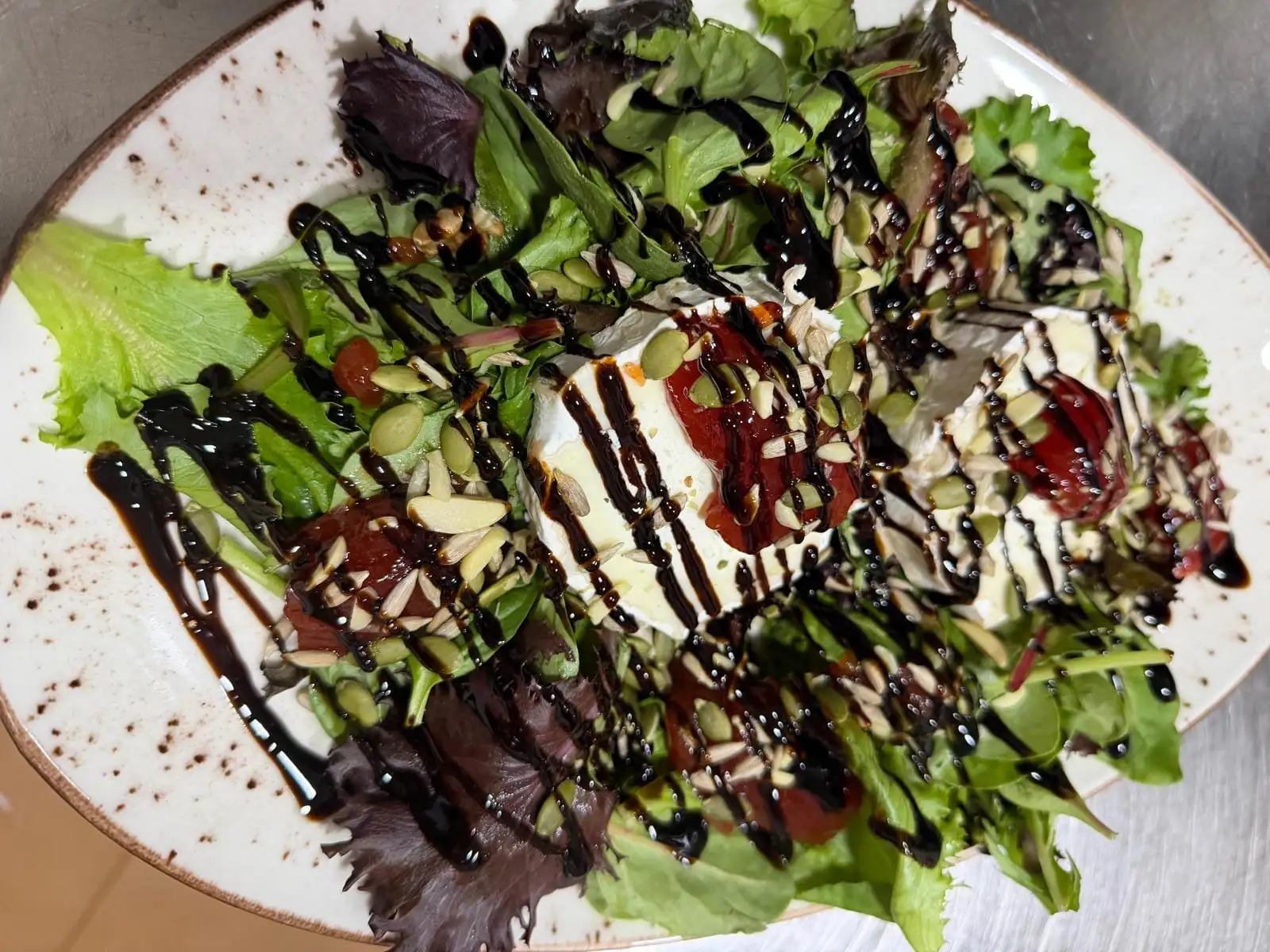 Ensalada de queso de cabra sobre brotes variados, con mermelada de tomate, pipas, almendra laminada y reducción de balsámico.