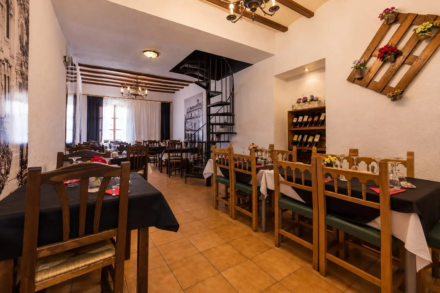 El salón de arriba visto a lo largo: dos filas de mesas vestidas de negro, la escalera de caracol en medio y un botellero de vino al fondo.