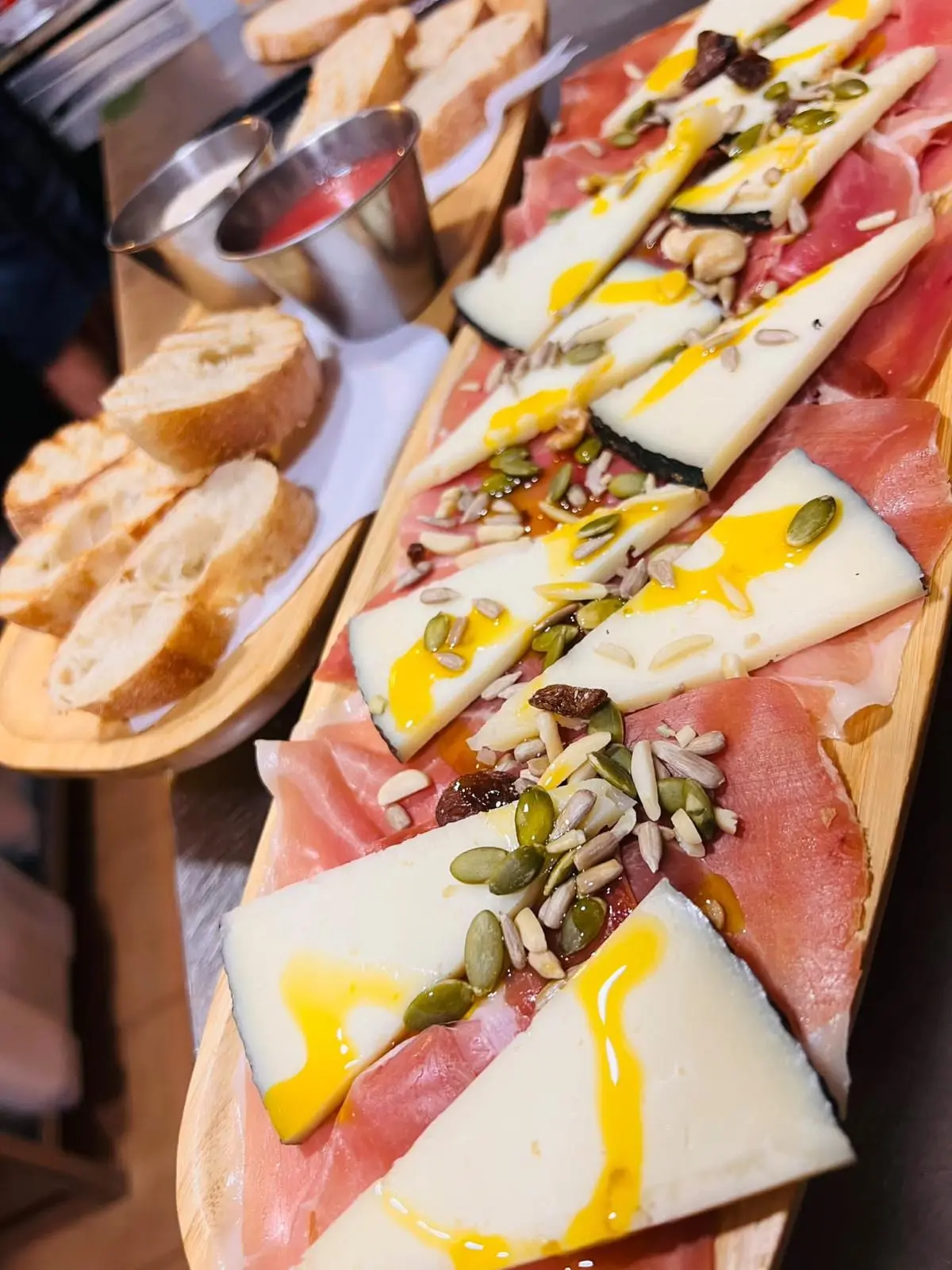 Tabla de jamón serrano y queso curado con frutos secos, un hilo de aceite y pan tostado al lado.
