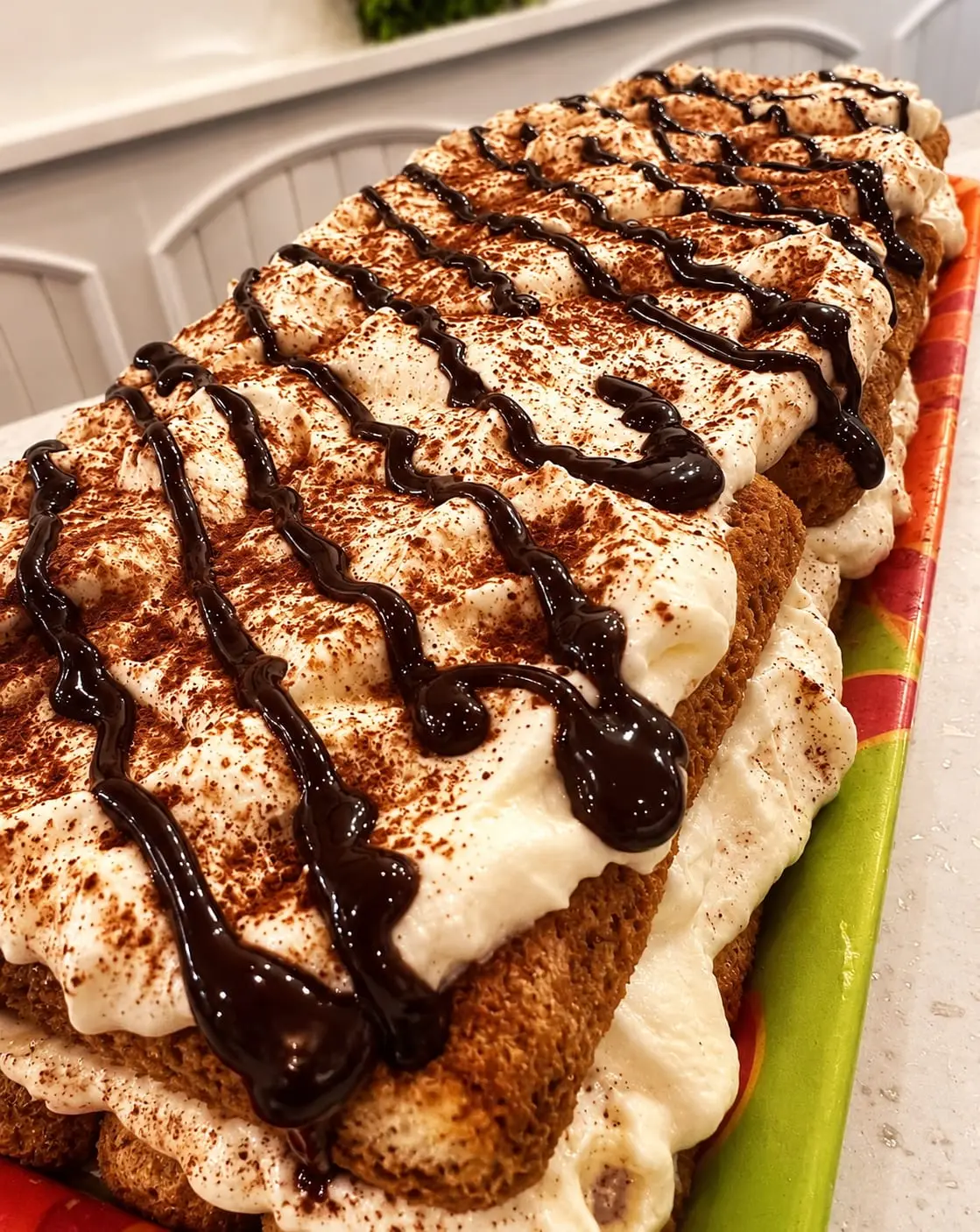 Bandeja de tiramisú recién montado, con la crema espolvoreada de cacao y un hilo de chocolate por encima.